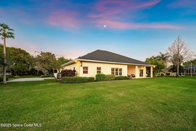 back of house at dusk with stucco siding and a lawn