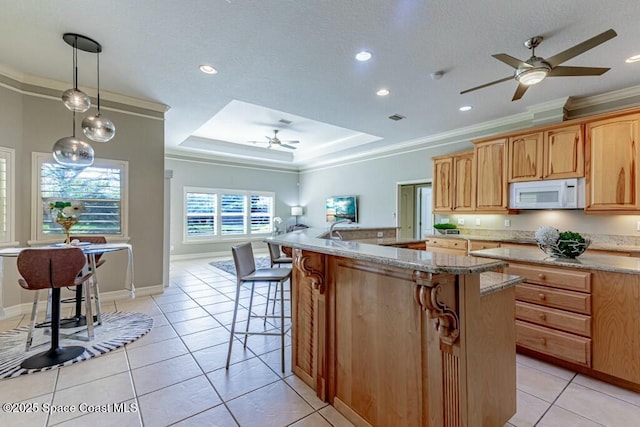 kitchen with light tile patterned floors, a ceiling fan, white microwave, ornamental molding, and a raised ceiling