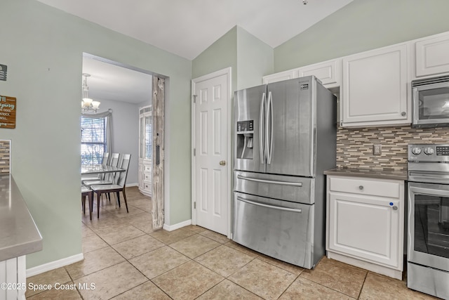 kitchen with lofted ceiling, decorative backsplash, stainless steel appliances, a notable chandelier, and white cabinetry