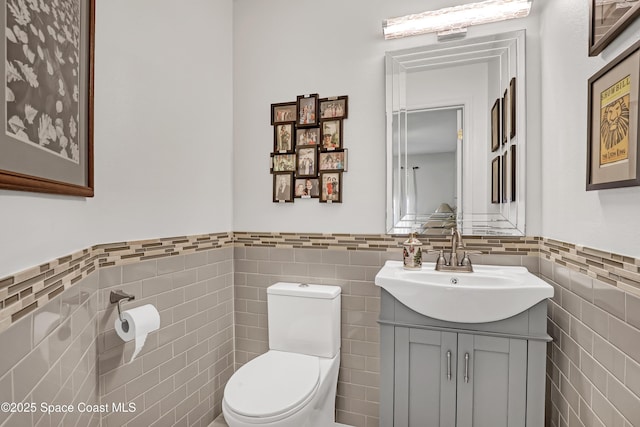 half bathroom featuring vanity, tile walls, toilet, and a wainscoted wall