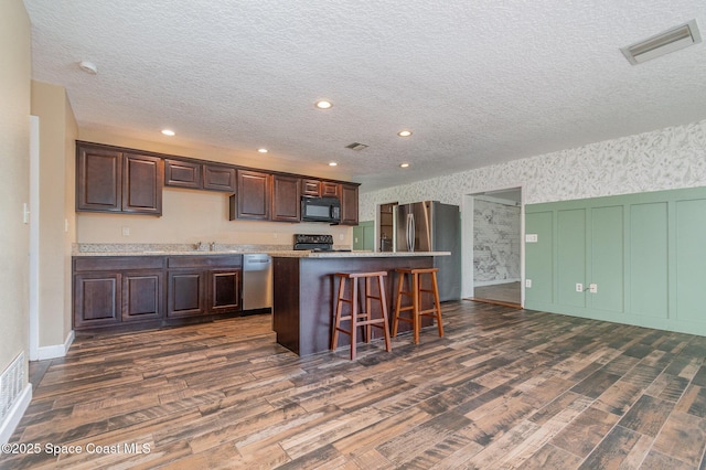 kitchen with visible vents, black appliances, a kitchen island, dark brown cabinetry, and wallpapered walls