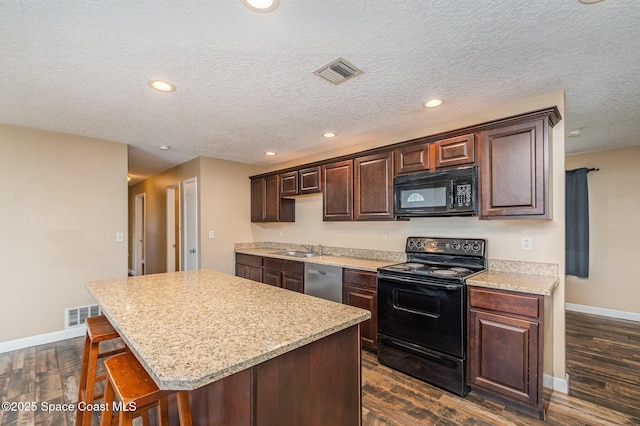 kitchen with visible vents, a center island, dark brown cabinetry, black appliances, and a sink