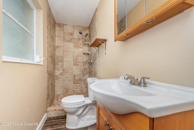 bathroom featuring toilet, a textured ceiling, wood finished floors, tiled shower, and vanity