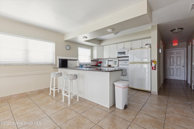 kitchen featuring light tile patterned floors, white cabinets, white appliances, and a peninsula