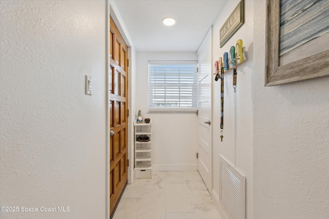 corridor featuring visible vents, baseboards, marble finish floor, and a textured wall