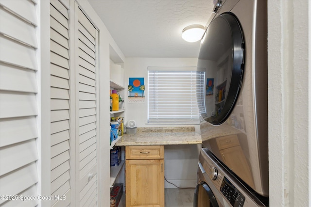 laundry area featuring cabinet space, a textured ceiling, and stacked washer and dryer