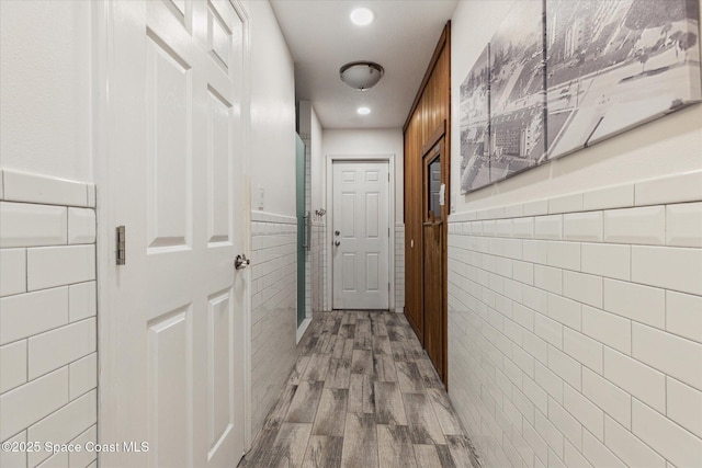 corridor featuring recessed lighting, a wainscoted wall, tile walls, and wood finished floors