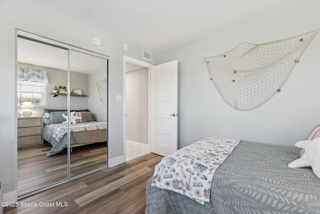 bedroom with wood finished floors, visible vents, a closet, and baseboards