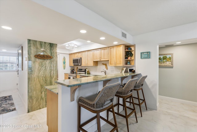 kitchen with decorative backsplash, a breakfast bar area, light brown cabinetry, and stainless steel appliances