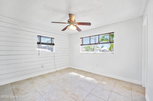 unfurnished room featuring a ceiling fan, a textured ceiling, wooden walls, light tile patterned floors, and baseboards