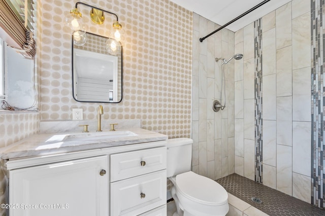 bathroom with vanity, toilet, a tile shower, and wallpapered walls