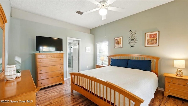 bedroom with a textured ceiling, ensuite bathroom, a ceiling fan, and wood finished floors