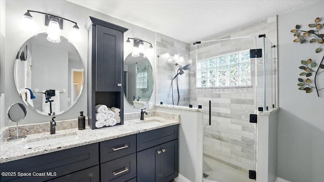 full bathroom with a sink, a textured ceiling, double vanity, and a shower stall