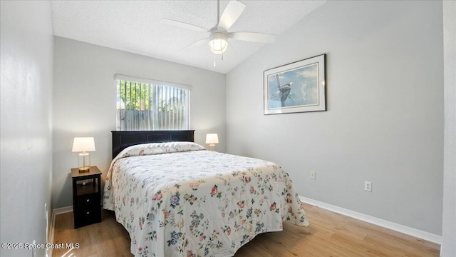 bedroom with a ceiling fan, baseboards, vaulted ceiling, a textured ceiling, and light wood-type flooring