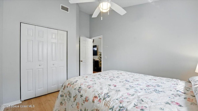 bedroom with visible vents, light wood-type flooring, vaulted ceiling, a closet, and a ceiling fan