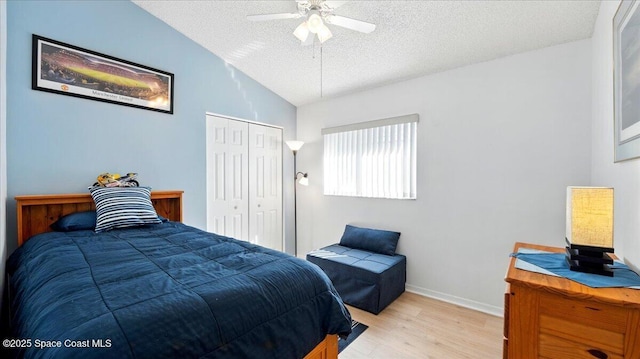 bedroom with light wood-style flooring, a textured ceiling, a closet, baseboards, and lofted ceiling