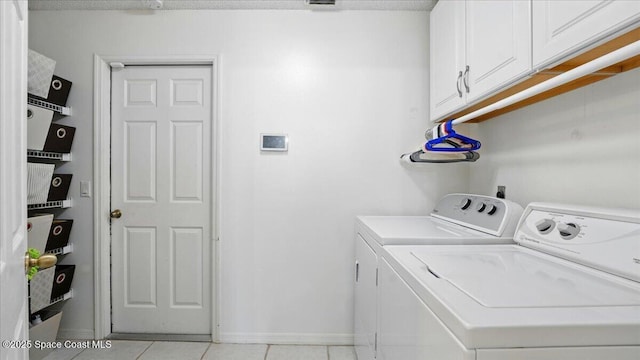 clothes washing area with light tile patterned flooring, cabinet space, baseboards, and washing machine and clothes dryer