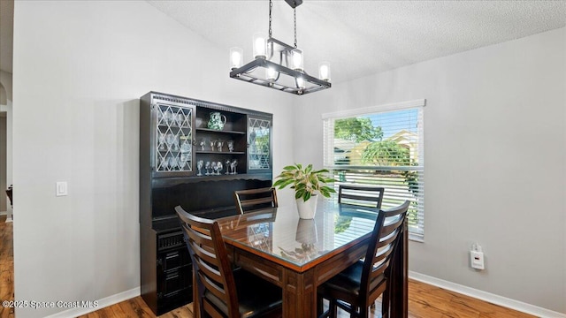 dining area with baseboards, a textured ceiling, an inviting chandelier, and wood finished floors