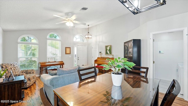 dining space with visible vents, ceiling fan with notable chandelier, a textured ceiling, wood finished floors, and vaulted ceiling