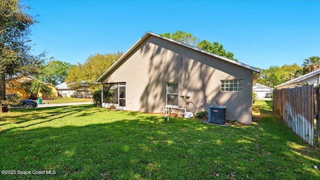 back of property with central AC unit, stucco siding, a yard, and fence