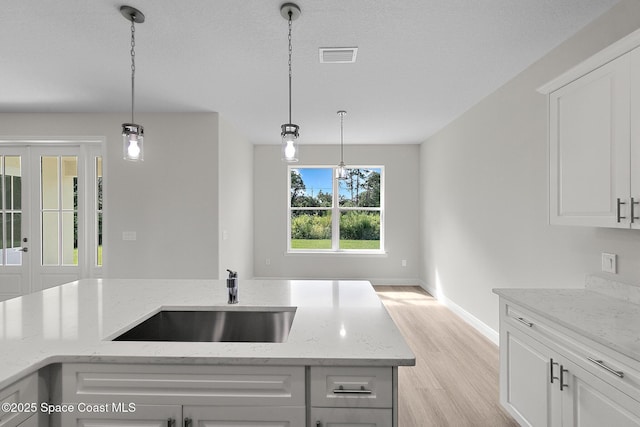 kitchen featuring visible vents, pendant lighting, light wood-type flooring, and a sink