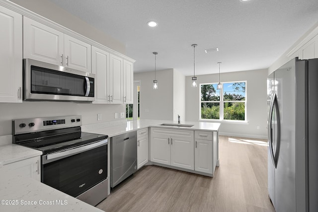 kitchen with appliances with stainless steel finishes, white cabinetry, a peninsula, and a sink