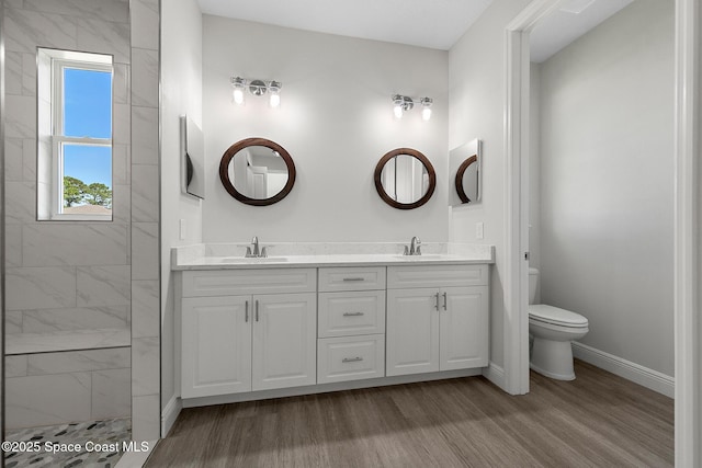 bathroom featuring wood finished floors, toilet, walk in shower, and a sink