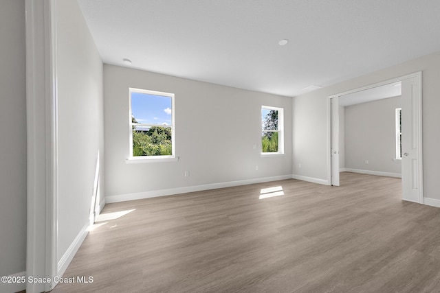 empty room featuring plenty of natural light, baseboards, and light wood-style floors