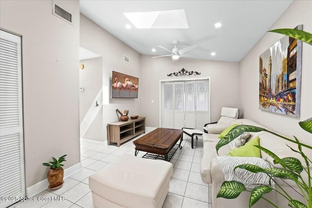 living room featuring vaulted ceiling with skylight, light tile patterned floors, visible vents, and ceiling fan