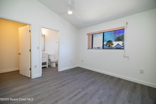 unfurnished bedroom featuring wood finished floors, baseboards, ensuite bath, vaulted ceiling, and a textured ceiling