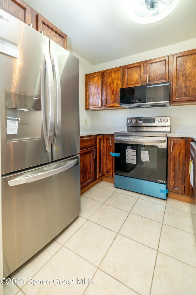 kitchen featuring light tile patterned floors, stainless steel appliances, brown cabinets, and light countertops