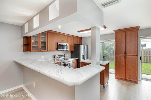 211 Cherie Down Ln, Cape Canaveral, FL 32920 - kitchen with appliances with stainless steel finishes, brown cabinetry, a peninsula, light wood-style floors, and glass insert cabinets