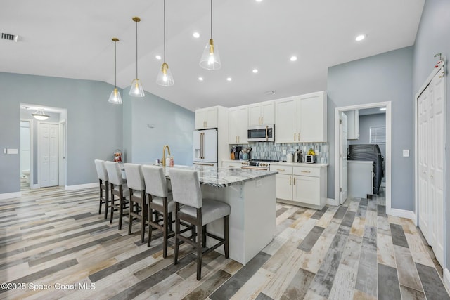 kitchen featuring high end appliances, an island with sink, white cabinets, a kitchen breakfast bar, and tasteful backsplash