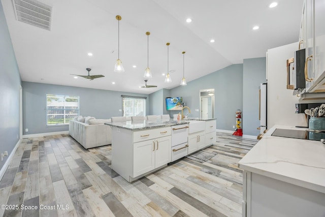 kitchen featuring visible vents, open floor plan, white cabinetry, fridge, and vaulted ceiling