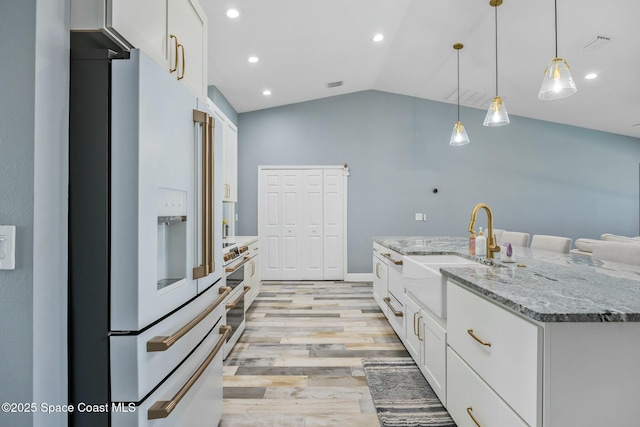 kitchen with light wood finished floors, lofted ceiling, premium appliances, white cabinets, and a sink