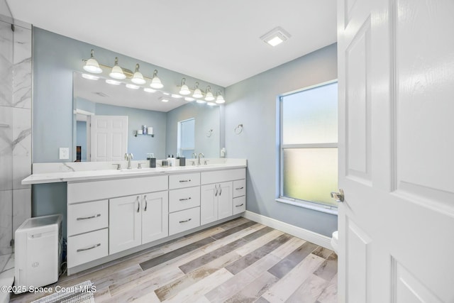 bathroom with baseboards, toilet, double vanity, wood finished floors, and a sink