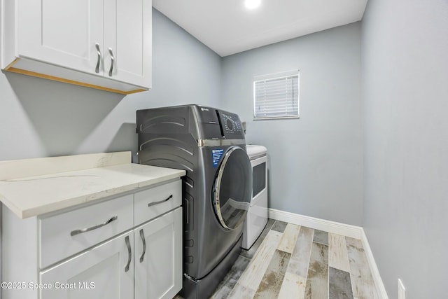 laundry room featuring baseboards, cabinet space, light wood-style floors, and independent washer and dryer