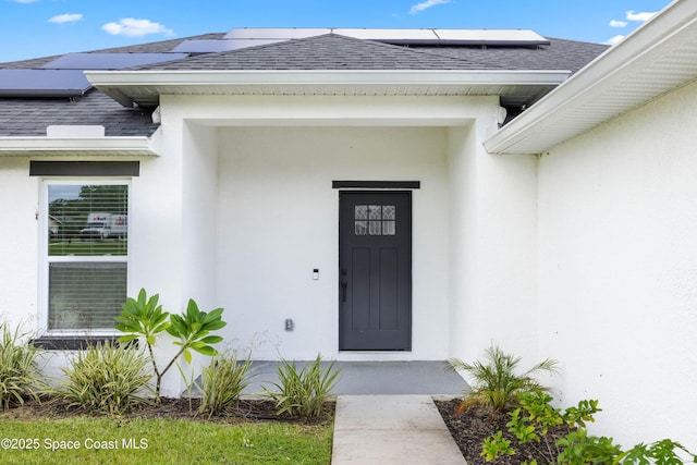 doorway to property with roof mounted solar panels, stucco siding, and roof with shingles