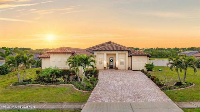 mediterranean / spanish house featuring fence, a yard, stucco siding, a tile roof, and decorative driveway