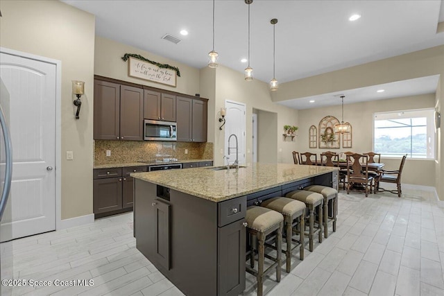 kitchen featuring light stone countertops, a sink, stainless steel microwave, a kitchen breakfast bar, and tasteful backsplash