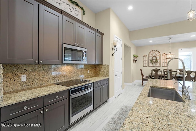 kitchen with a sink, decorative light fixtures, backsplash, stainless steel appliances, and light stone countertops