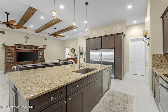 kitchen featuring beamed ceiling, a kitchen island with sink, a ceiling fan, a sink, and open floor plan