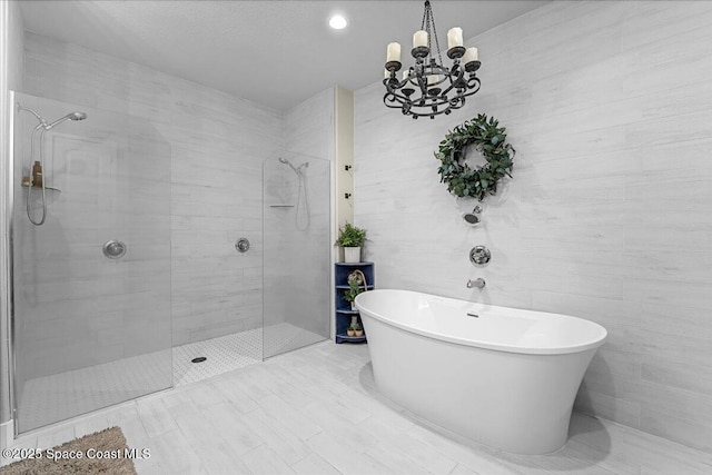 bathroom with a notable chandelier, a freestanding bath, tiled shower, and tile walls