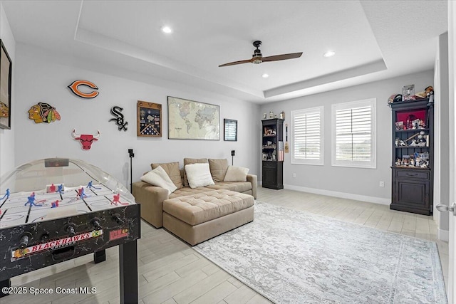 living area featuring baseboards, light wood-type flooring, recessed lighting, a raised ceiling, and a ceiling fan