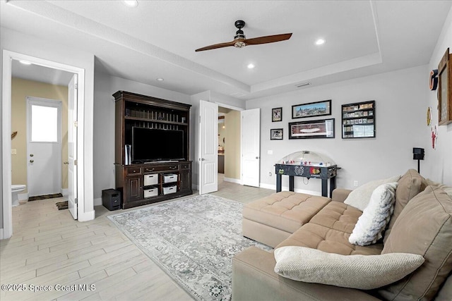 living room featuring light wood-type flooring, a tray ceiling, baseboards, and a ceiling fan