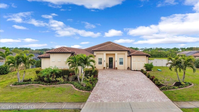 mediterranean / spanish-style house with fence, stucco siding, a front lawn, a tiled roof, and decorative driveway