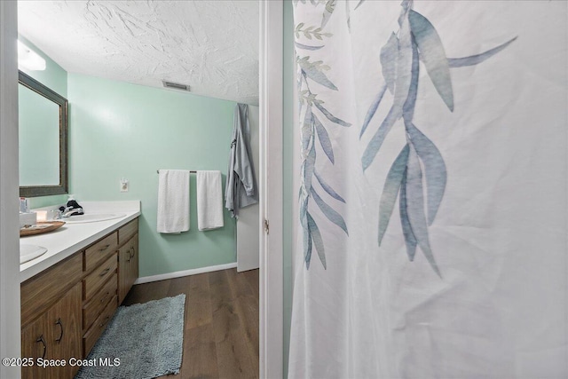 full bathroom featuring visible vents, a sink, a textured ceiling, wood finished floors, and double vanity