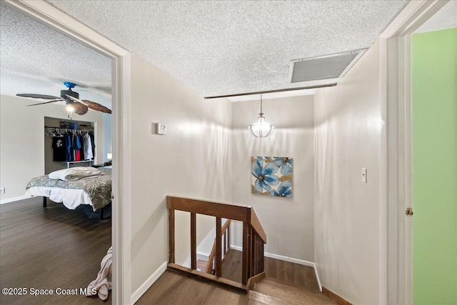 hallway featuring visible vents, a textured ceiling, baseboards, and wood finished floors