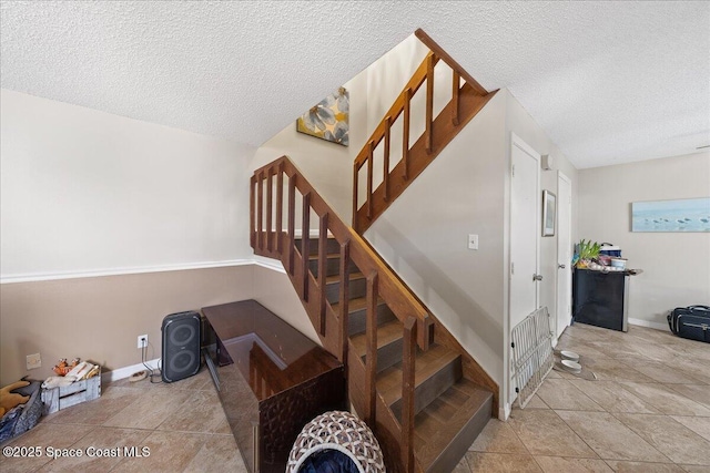 staircase with tile patterned floors, a textured ceiling, and baseboards