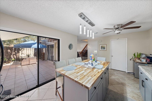 kitchen featuring wood counters, a textured ceiling, a center island, and a ceiling fan